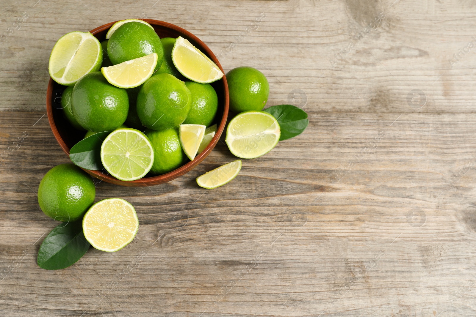 Photo of Tasty ripe limes in bowl on wooden table, top view