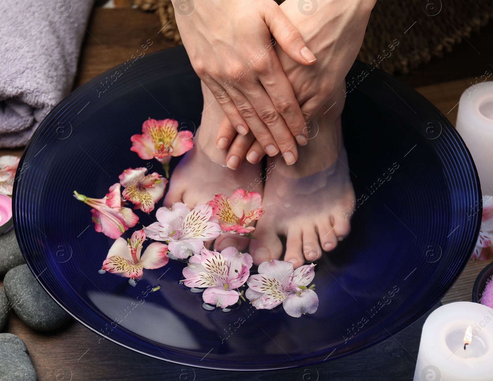 Photo of Woman soaking her feet in bowl with water and flowers on floor, closeup. Spa treatment