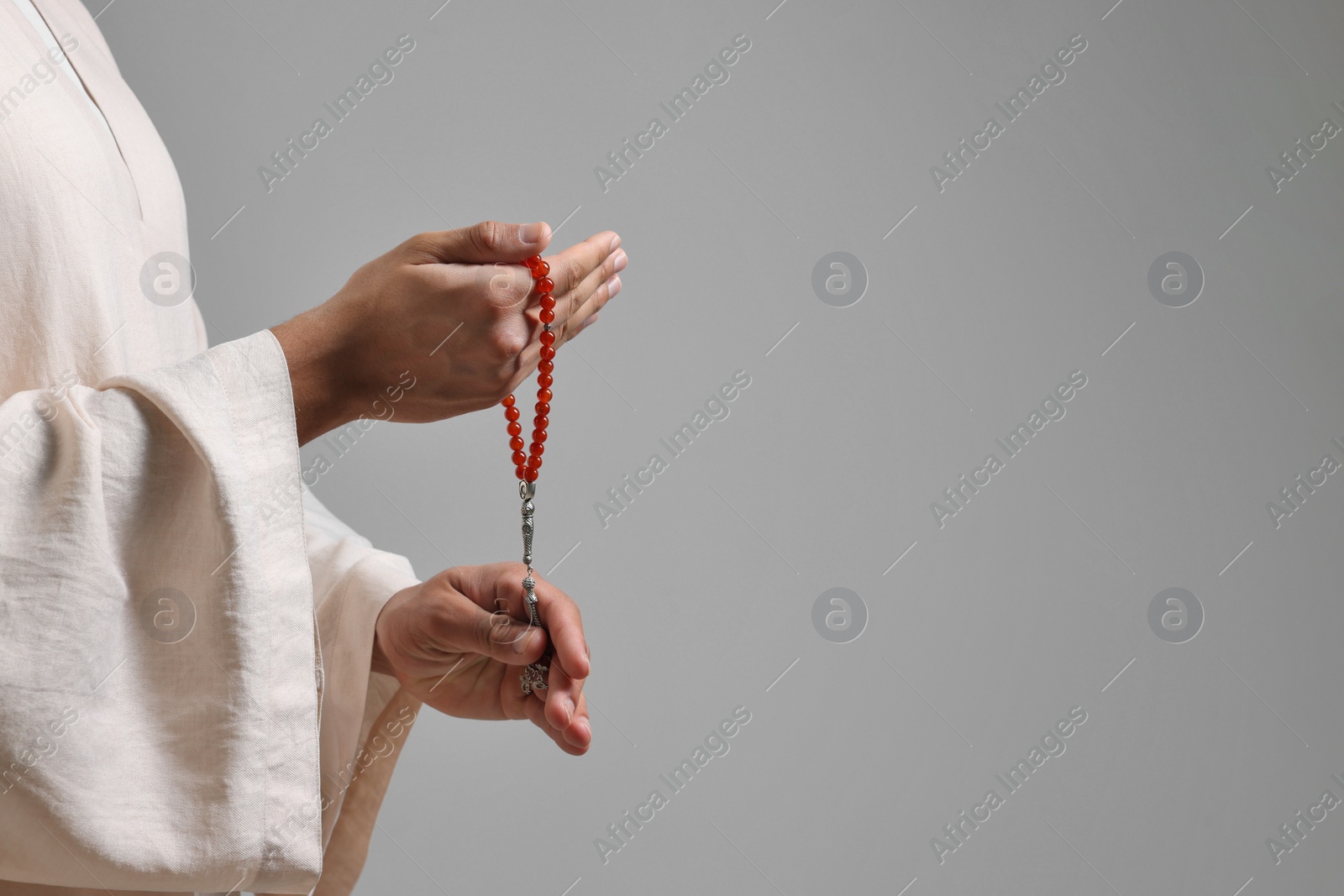 Photo of Muslim man with misbaha on light grey background, closeup. Space for text