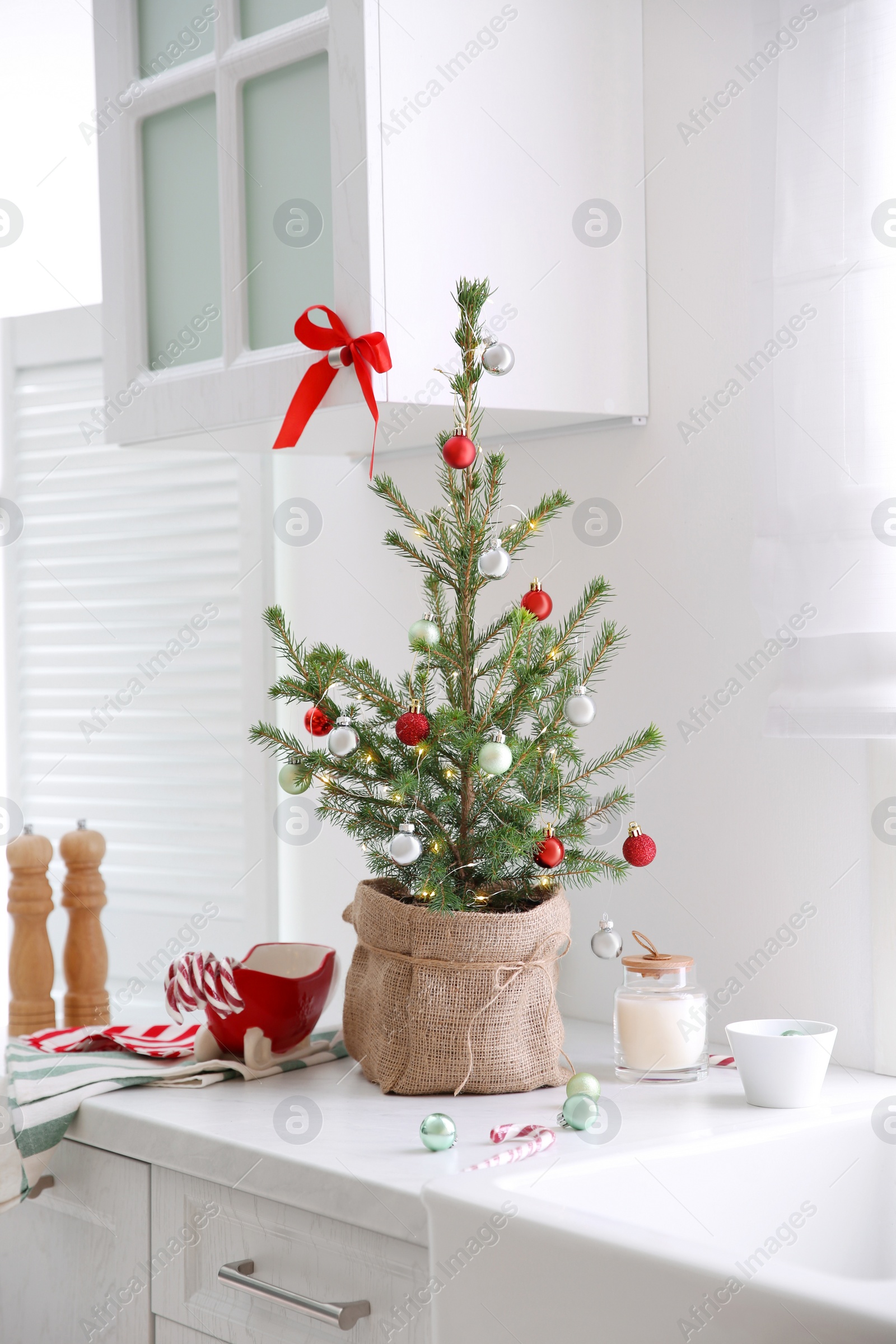 Photo of Small Christmas tree decorated with baubles and festive lights in kitchen