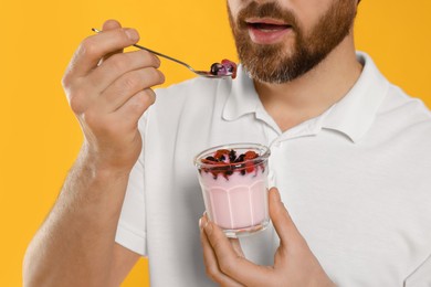 Man eating delicious yogurt on yellow background, closeup