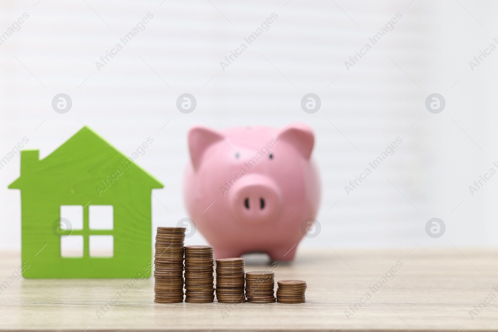 Photo of House model, piggy bank and stacked coins on wooden table, selective focus