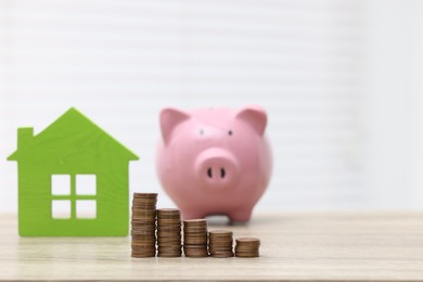 House model, piggy bank and stacked coins on wooden table, selective focus