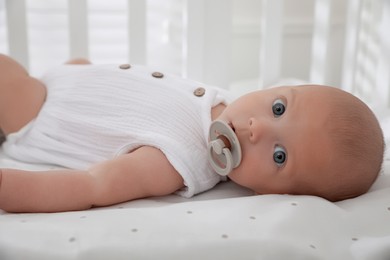 Photo of Cute little baby with pacifier lying on bed, closeup