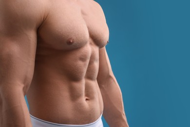 Photo of Muscular man showing abs on light blue background, closeup and space for text. Sexy body