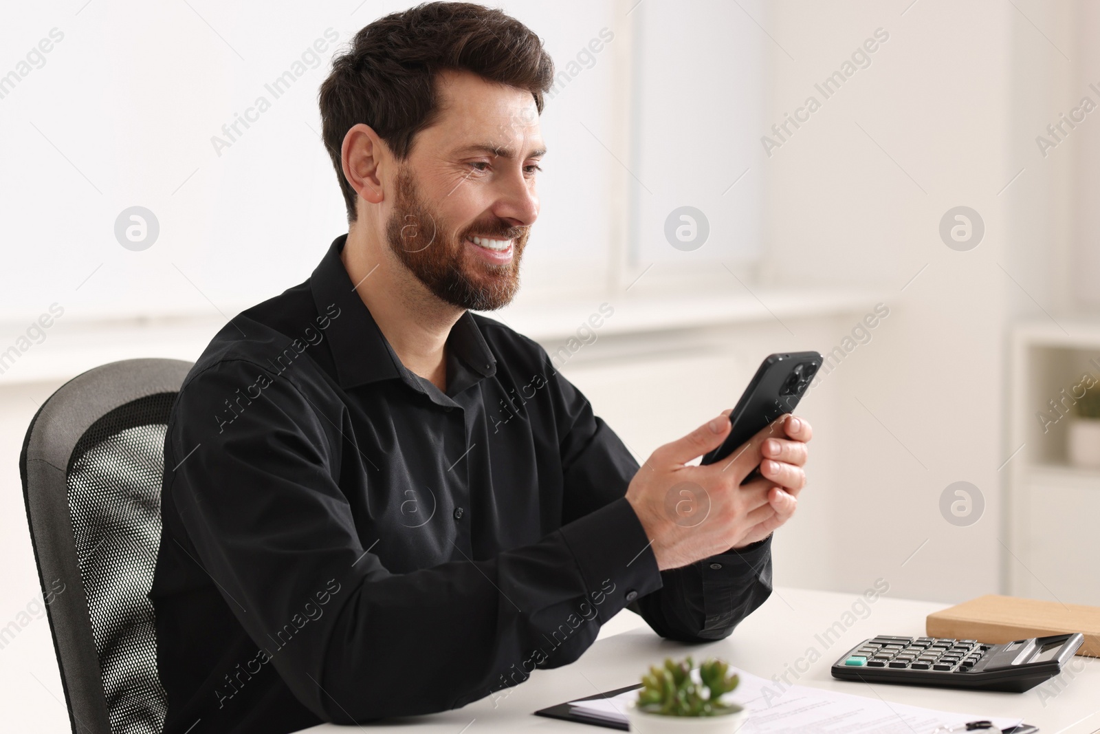 Photo of Smiling man using smartphone at table in office