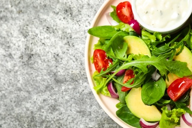 Photo of Delicious salad with tomatoes, arugula and avocado on grey table, top view. Space for text
