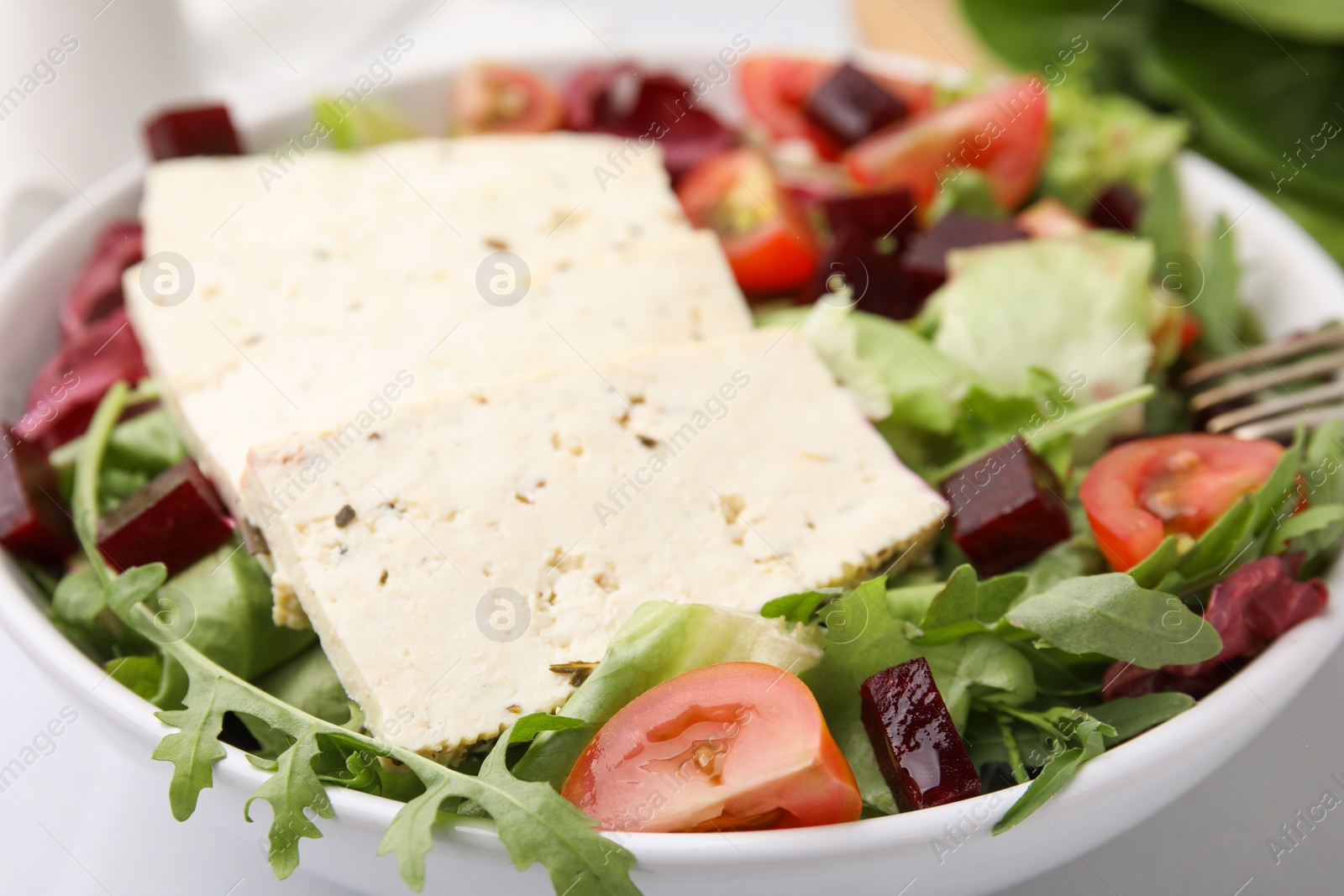 Photo of Bowl of tasty salad with tofu and vegetables on table, closeup