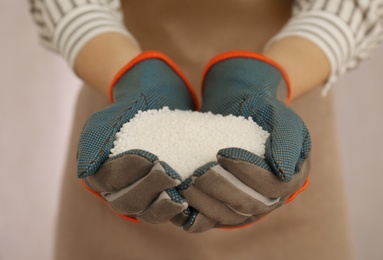 Photo of Woman holding pile of granular mineral fertilizer on light background, closeup