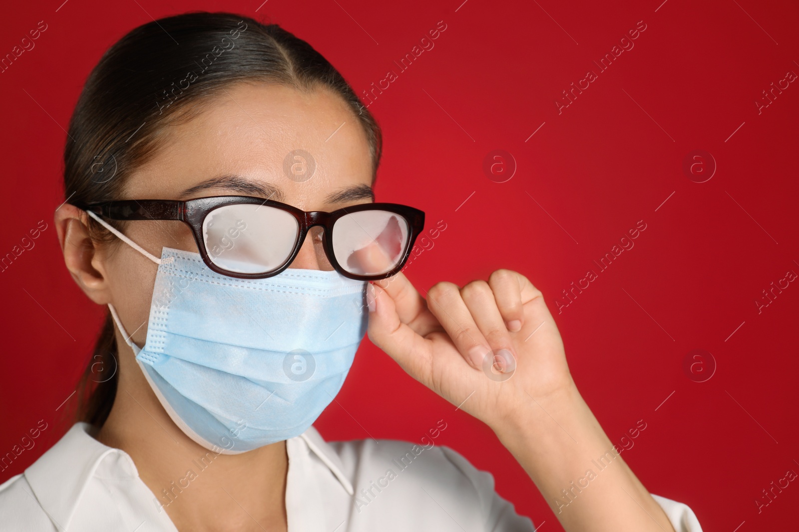 Photo of Woman wiping foggy glasses caused by wearing medical mask on red background, closeup