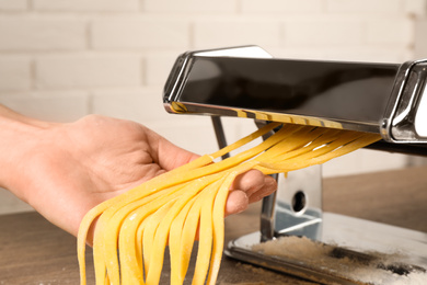Woman preparing noodles with pasta maker machine at wooden table, closeup
