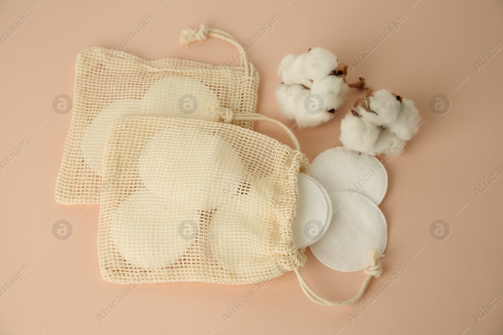 Photo of Bags with cotton pads and flowers on beige background, above view