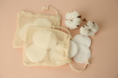 Photo of Bags with cotton pads and flowers on beige background, above view