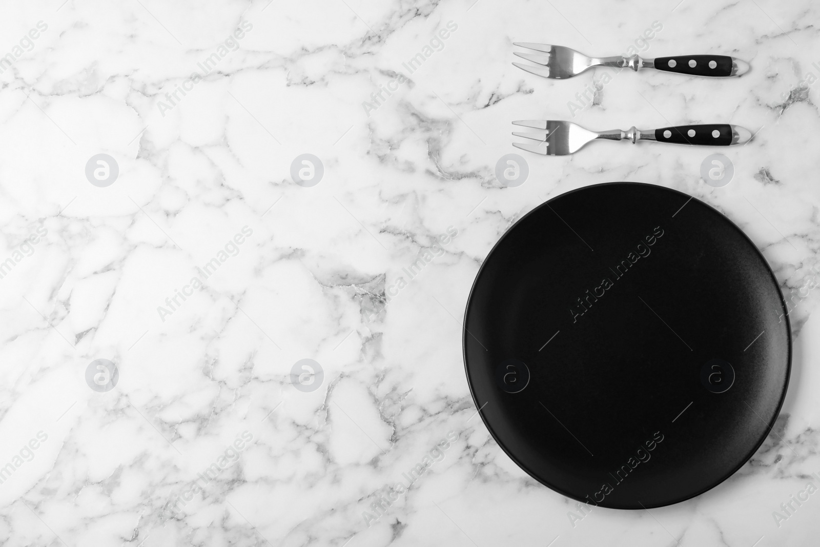 Photo of Forks and empty plate on marble table, flat lay with space for text