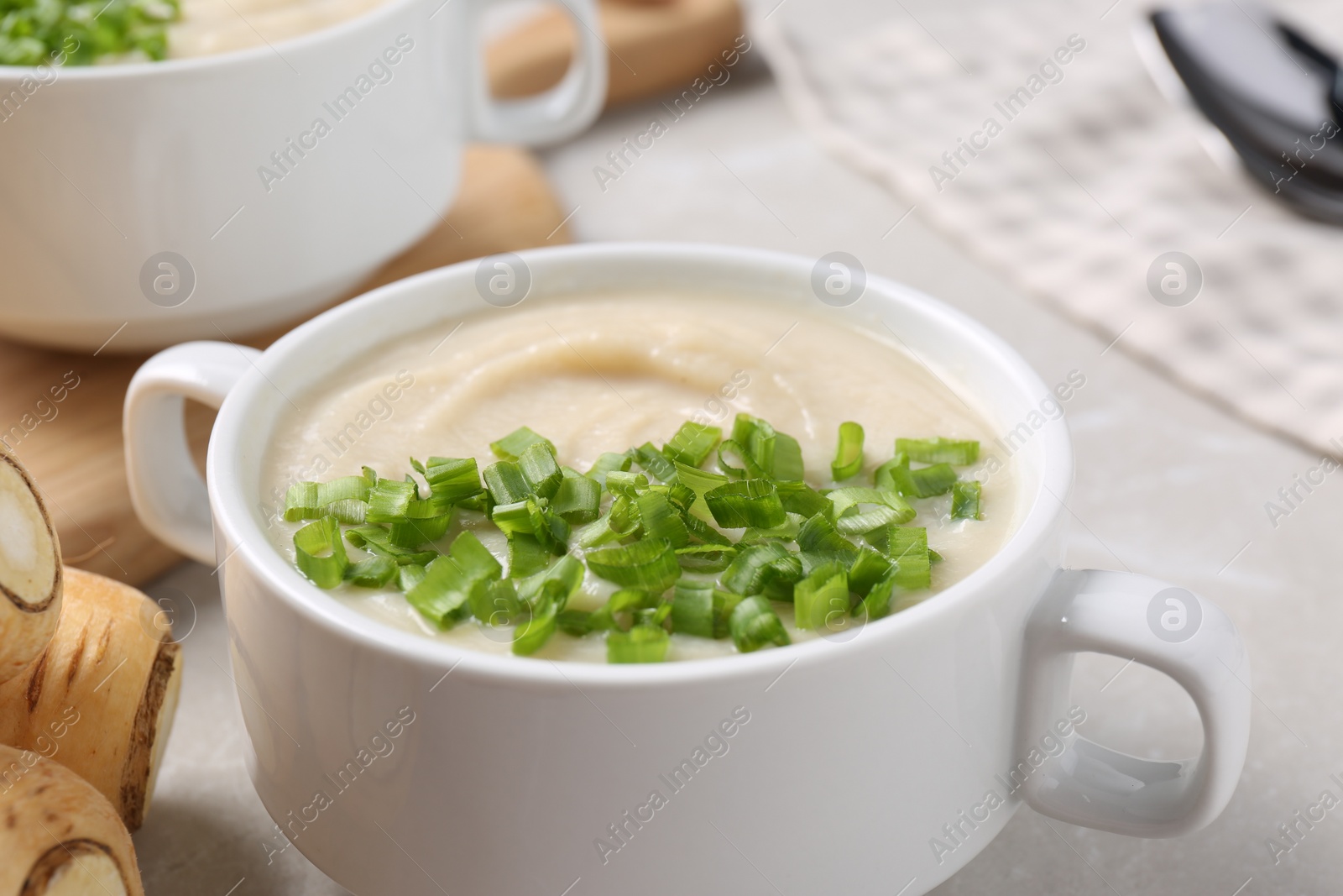 Photo of Bowl with tasty creamy soup of parsnip on light grey table, closeup