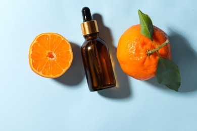 Aromatic tangerine essential oil in bottle and citrus fruits on light blue table, top view. Space for text