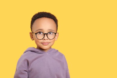 Photo of Cute African-American boy with glasses on yellow background. Space for text