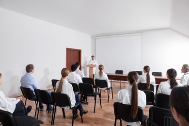 Photo of Doctor giving lecture in conference room with projection screen