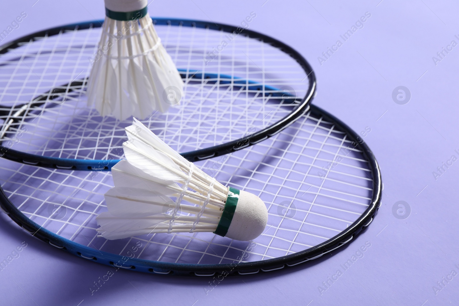 Photo of Feather badminton shuttlecocks and rackets on violet background, closeup