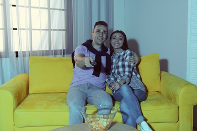 Happy young couple watching TV on sofa at home