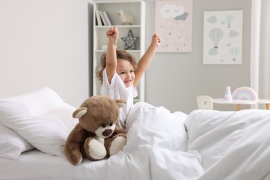Photo of Cute little girl stretching and teddy bear on bed at home
