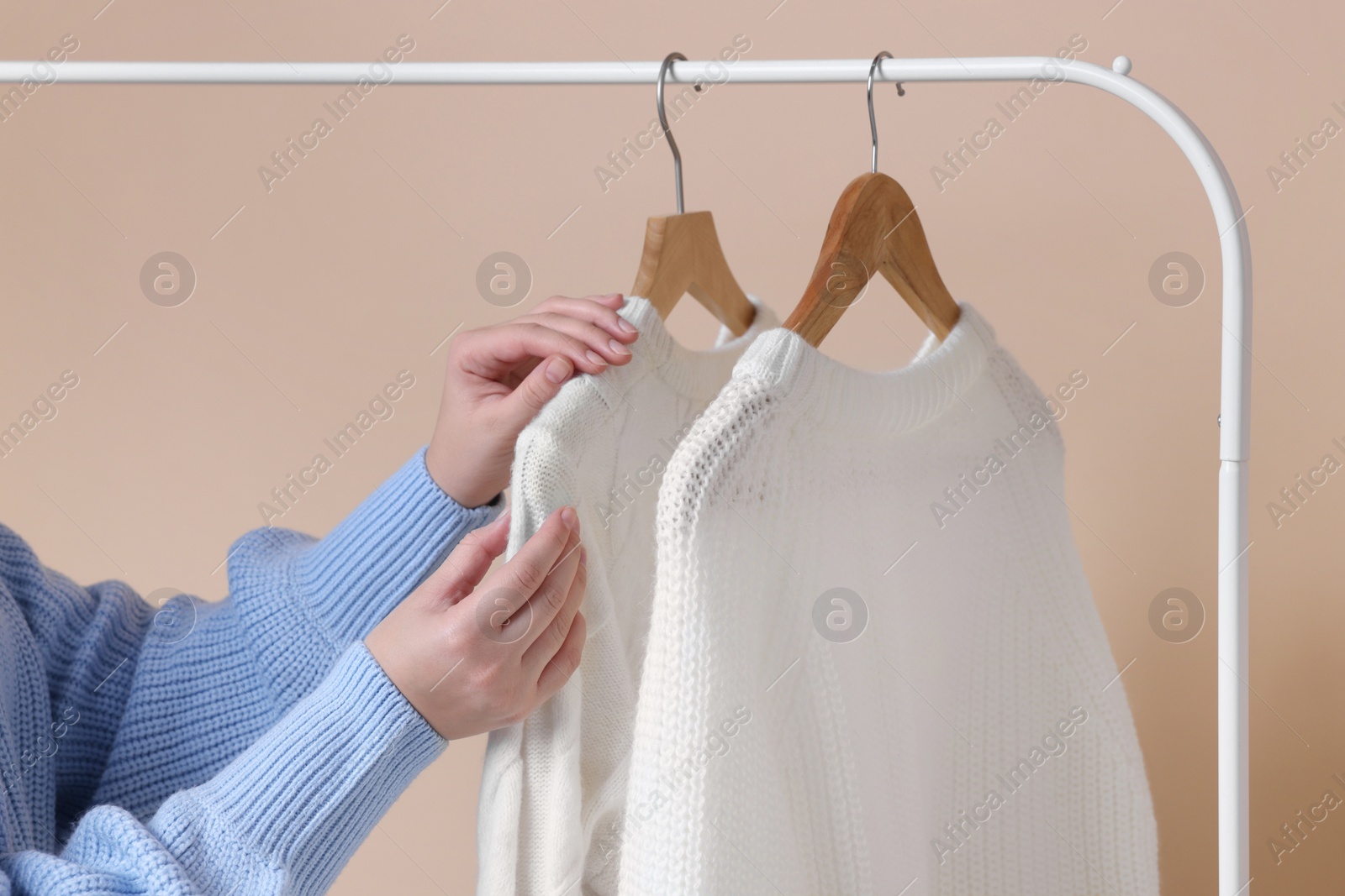 Photo of Woman taking sweater from rack on beige background, closeup