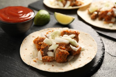 Photo of Delicious tacos with vegetables, meat and ketchup on grey table, closeup