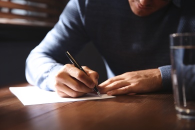 Photo of Man writing letter at wooden table indoors, closeup