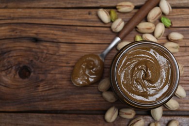 Tasty pistachio nut paste in jar and spoon on wooden table, flat lay. Space for text