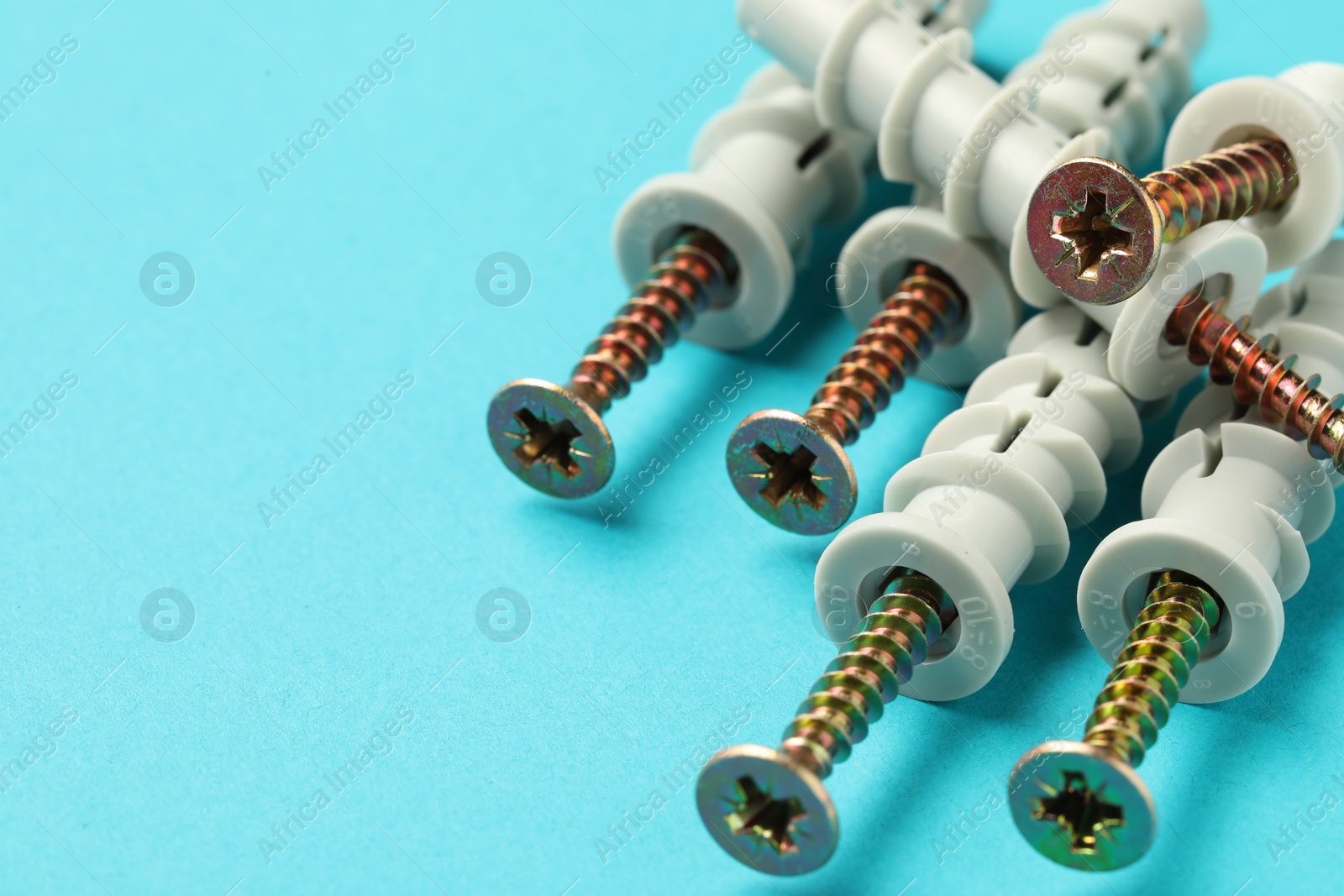 Photo of Many metal screws with dowels on light blue background, closeup. Space for text