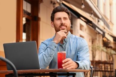 Photo of Man with drink and laptop at table in outdoor cafe