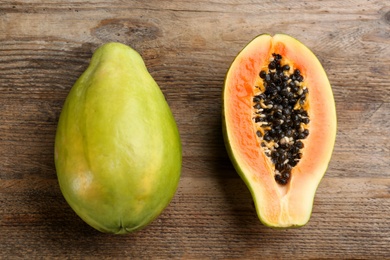 Photo of Cut and whole fresh ripe papaya fruits on wooden table, flat lay