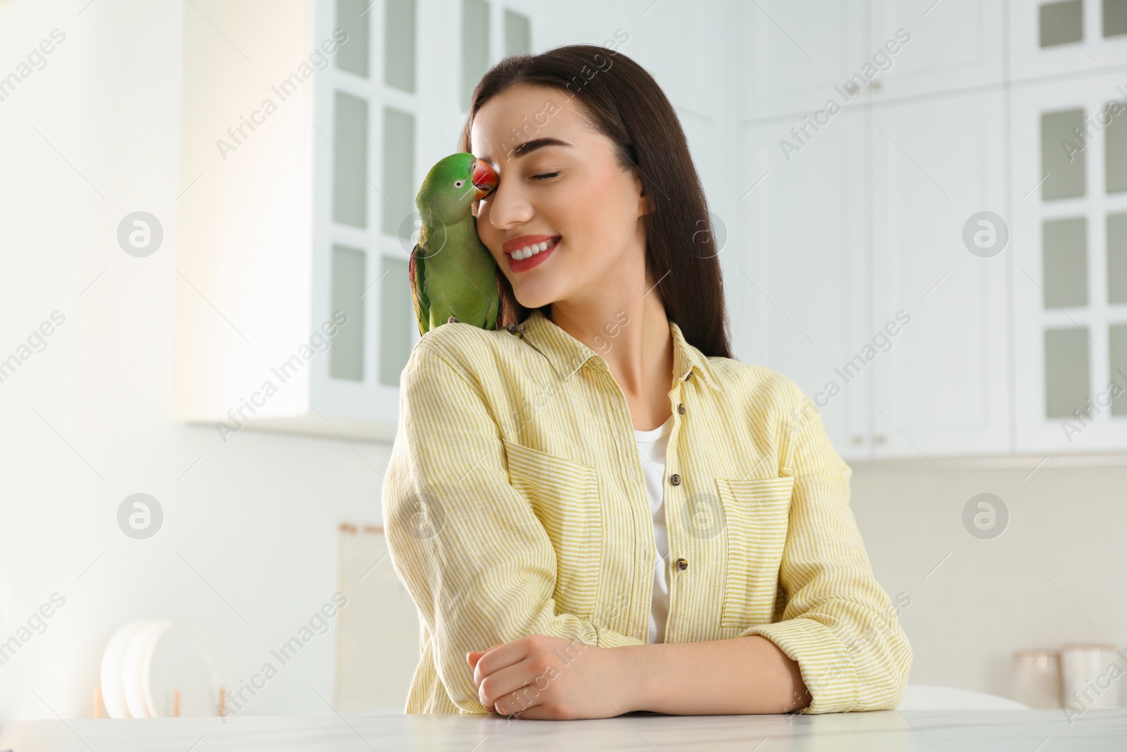 Photo of Young woman with Alexandrine parakeet indoors. Cute pet