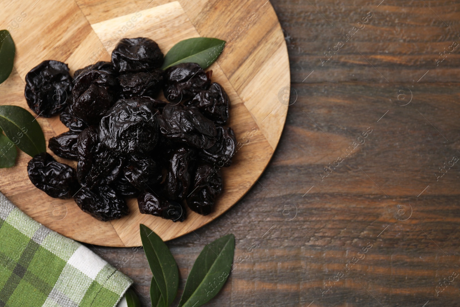 Photo of Tasty dried prunes and green leaves on wooden table, top view. Space for text