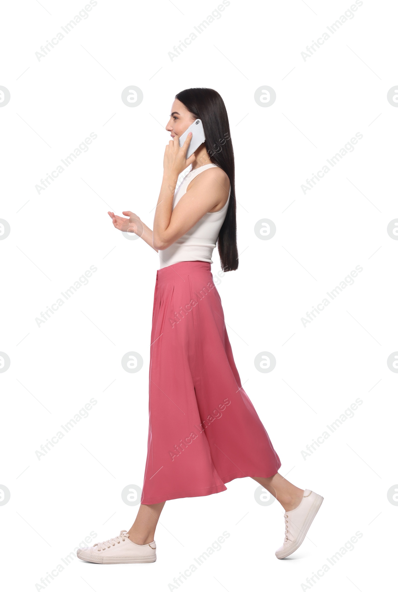 Photo of Young woman talking on smartphone while walking against white background