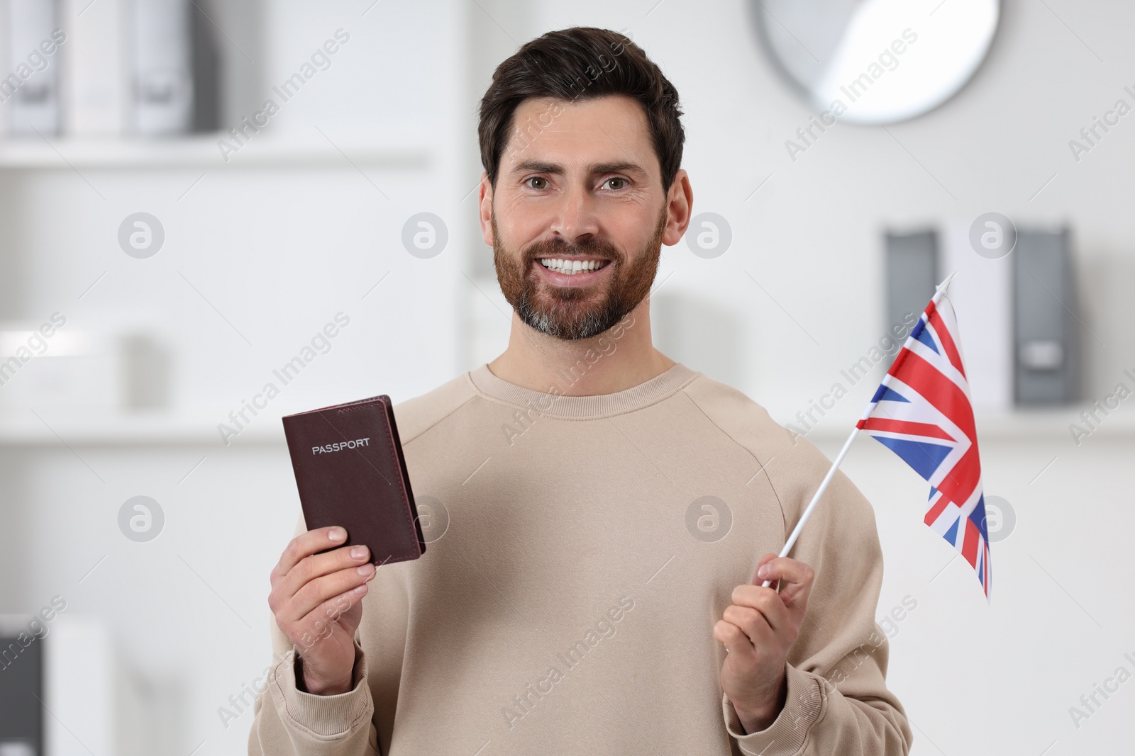 Photo of Immigration. Happy man with passport and flag of United Kingdom indoors