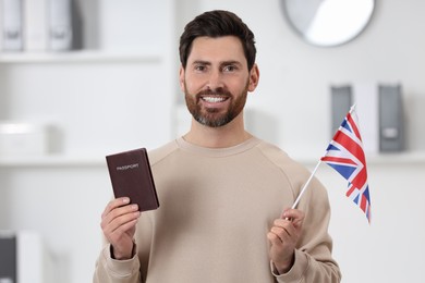 Photo of Immigration. Happy man with passport and flag of United Kingdom indoors