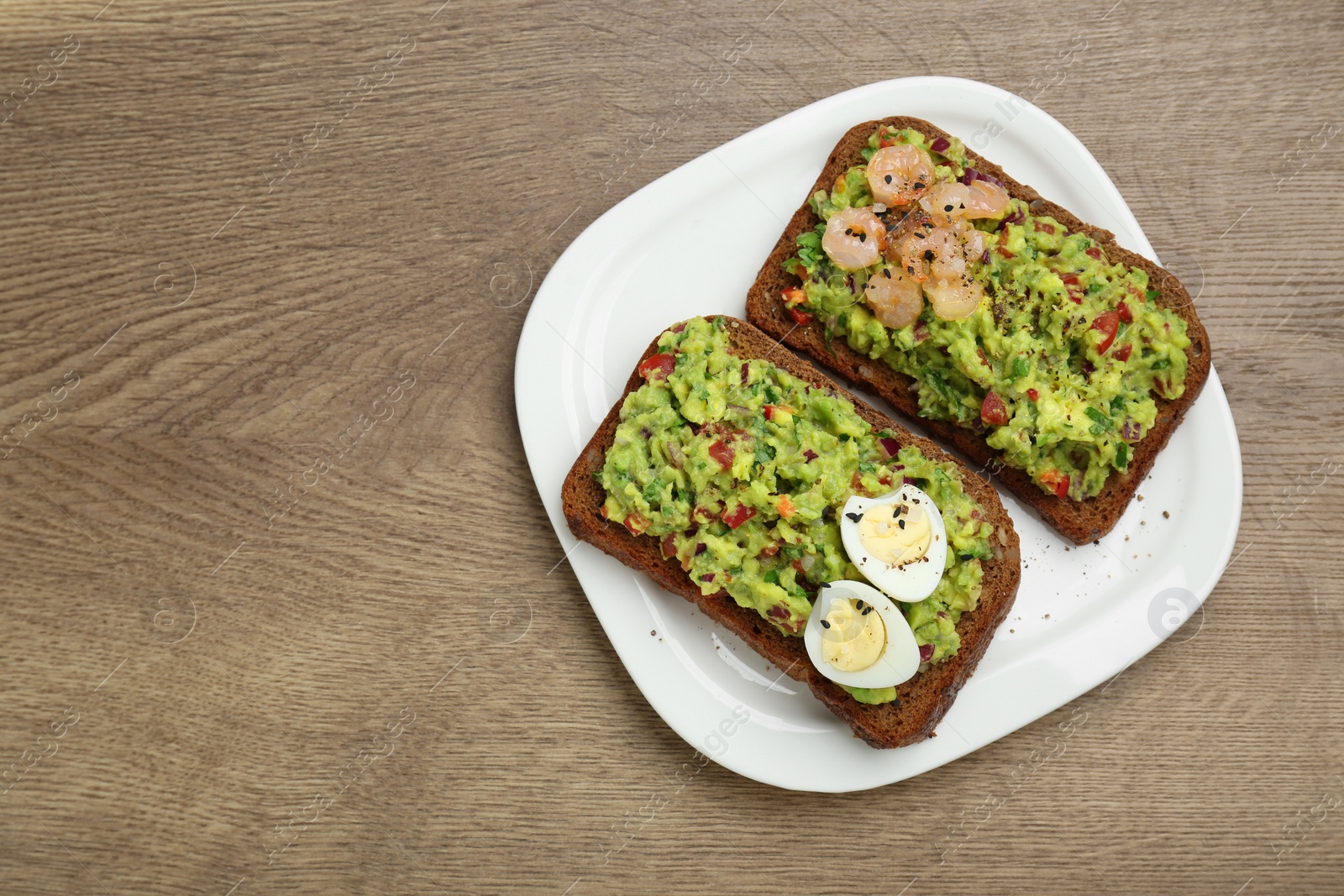 Photo of Slices of bread with tasty guacamole, eggs and shrimp on wooden table, top view. Space for text