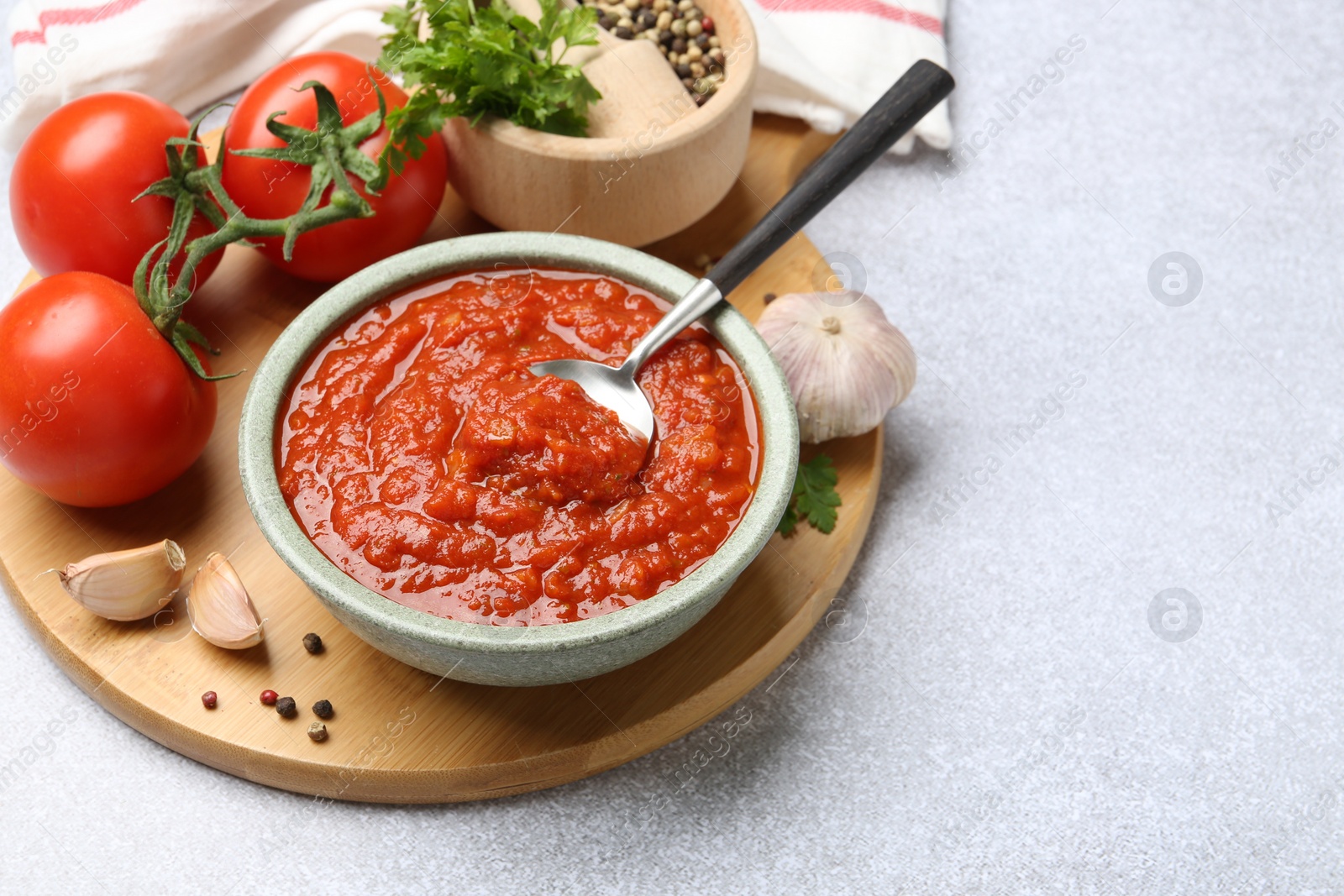 Photo of Homemade tomato sauce in bowl, spoon and fresh ingredients on light grey table. Space for text