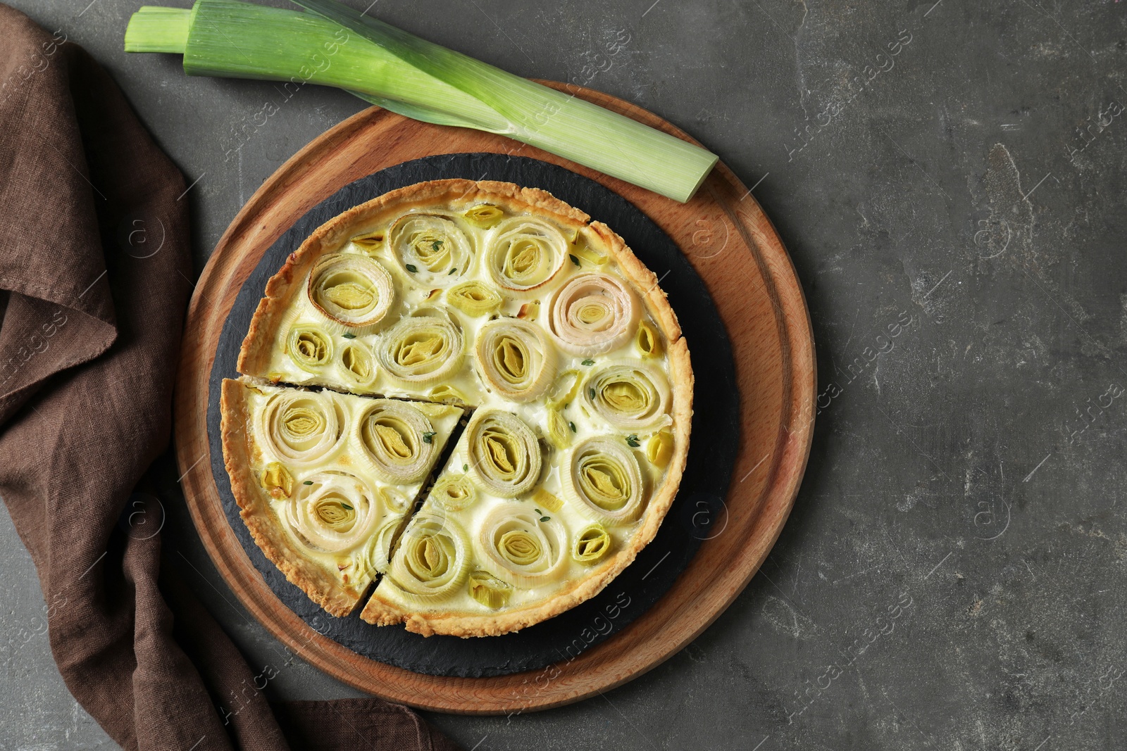 Photo of Tasty leek pie and fresh stalk on dark textured table, flat lay. Space for text