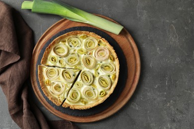 Photo of Tasty leek pie and fresh stalk on dark textured table, flat lay. Space for text