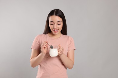 Happy woman with tasty yogurt on grey background