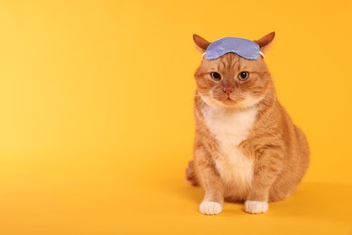 Photo of Cute ginger cat with sleep mask on orange background, space for text