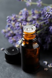 Photo of Bottle with essential oil near lavender on grey table, closeup