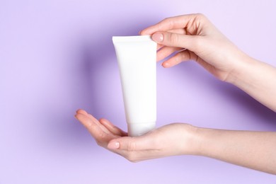 Woman holding tube of cream on violet background, closeup