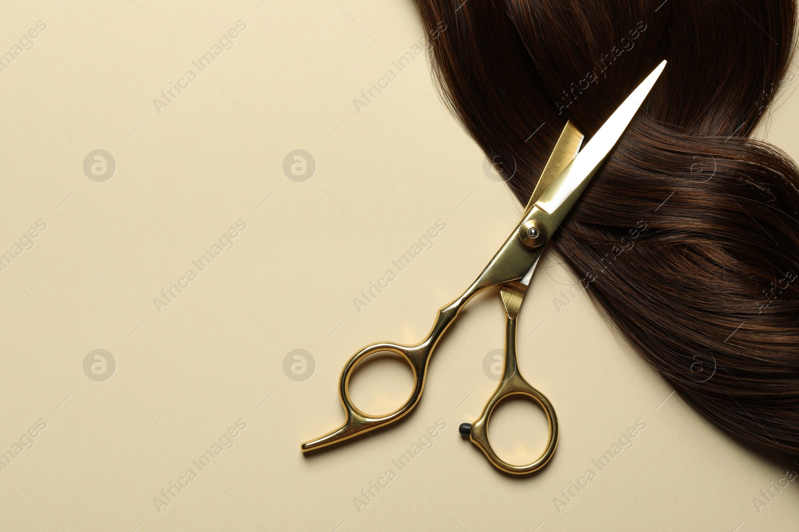 Photo of Professional scissors with brown hair strand on beige background, top view. Space for text