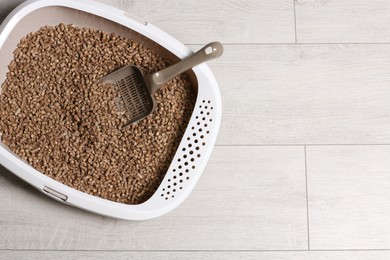 Photo of Cat tray with biodegradable litter and scoop on wooden floor, top view. Space for text