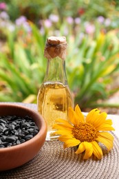 Photo of Bottle of sunflower oil and seeds in bowl on table outdoors
