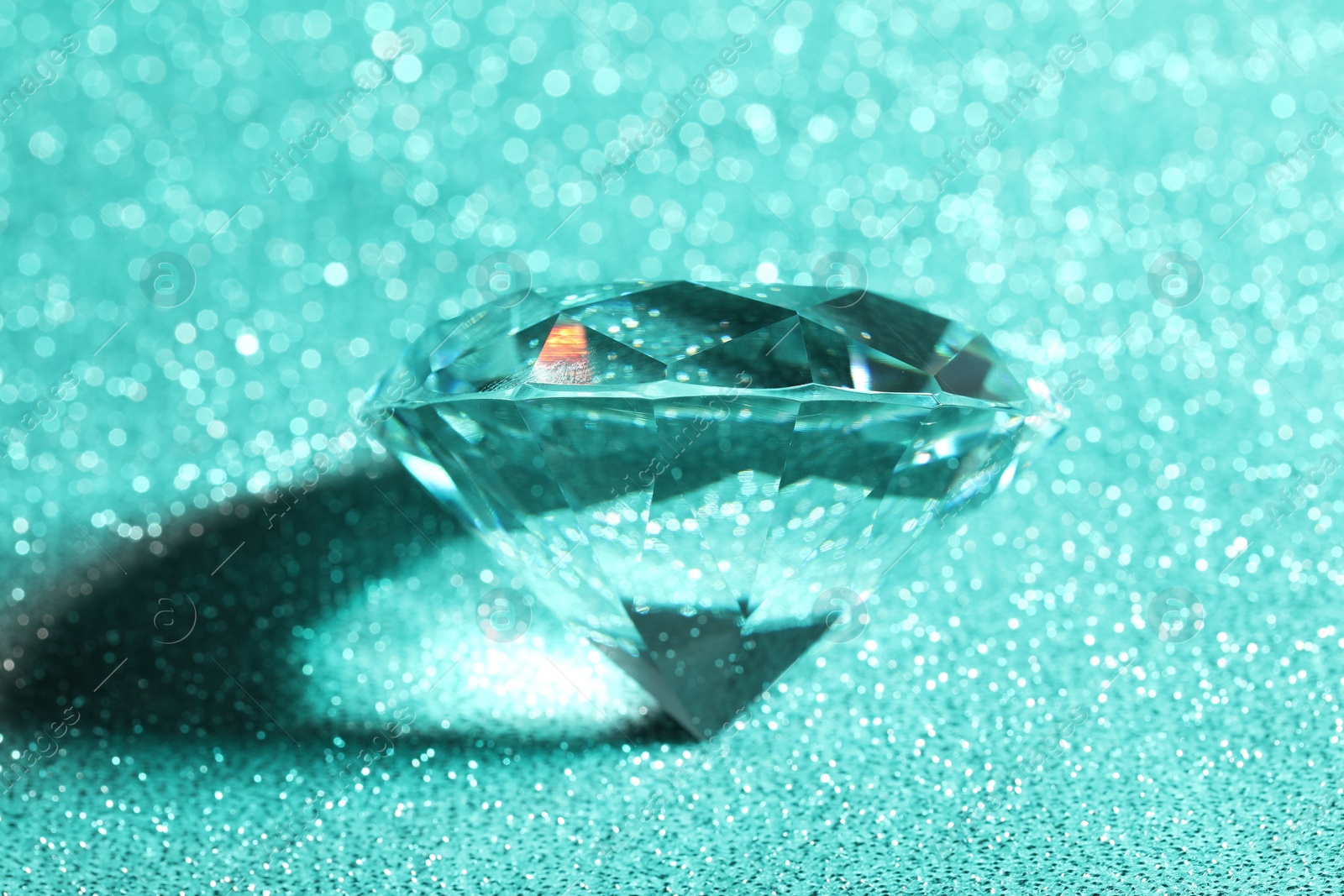 Photo of Beautiful dazzling diamond on green glitter background, closeup