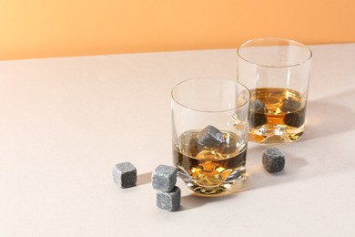 Whiskey stones and drink in glasses on light table. Space for text